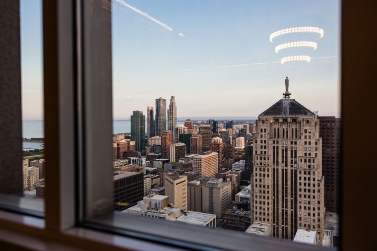 View through a window of the Chicago skyline, with an Art Deco tower topped by a statue and Lake Michigan beyond.